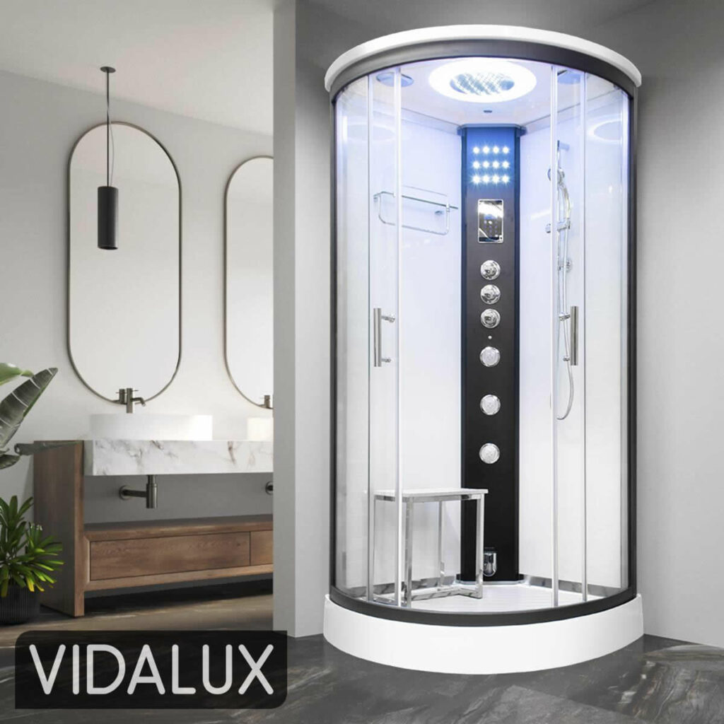 A Vidalux Essence quadrant steam shower with white back panels, a white seat and a white tray, showing its curved sliding glass doors with their handles and the closing edges where the seals sit, in a bathroom with oval mirrors