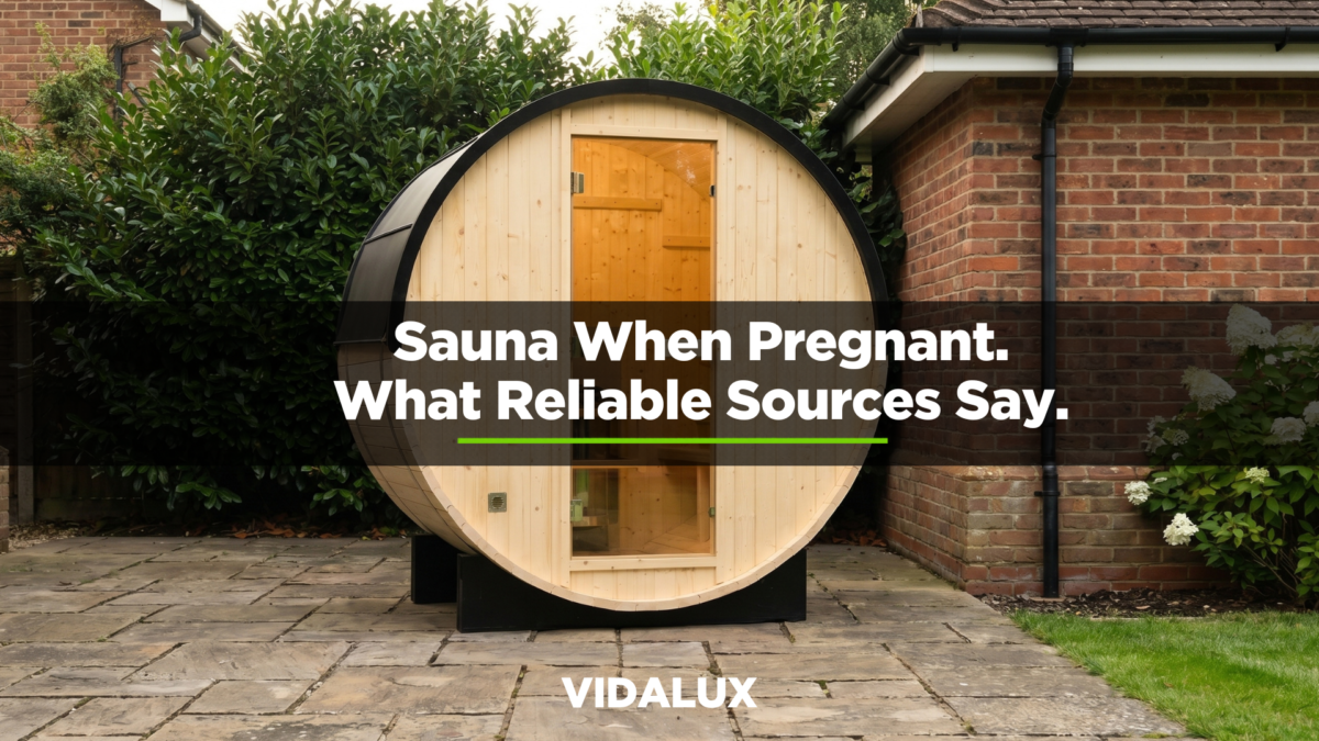 Vidalux outdoor barrel sauna installed on a stone-paved patio against a British residential brick house, surrounded by laurel hedging and white hydrangeas in warm late-afternoon light.