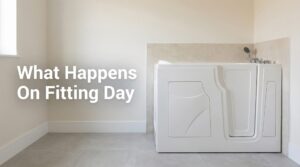 A compact white walk-in bath with an inward-opening door installed in a neutral bathroom setting, with right-hand chrome mixer taps and a handheld shower head on a wall holder. Headline overlay reads: What Happens On Fitting Day.