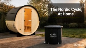 A wooden Vidalux home sauna and a Vidalux Therapy Pod ice bath set up together on a deck in a UK back garden, lit by warm late afternoon sunlight.