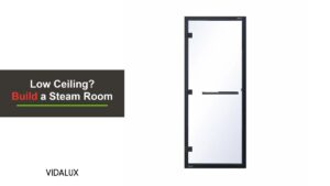 The Vidalux 1860mm by 780mm clear glass steam room door with a black frame, black hinges and a black bar handle, shown against white.